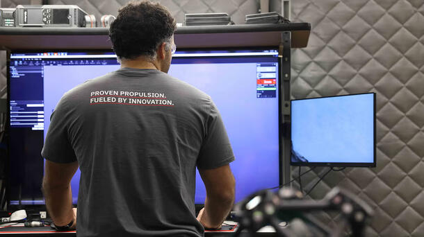 An employee looks at his screen in a T-shirt that says "Proven Propulsion. Fueled by Innovation."